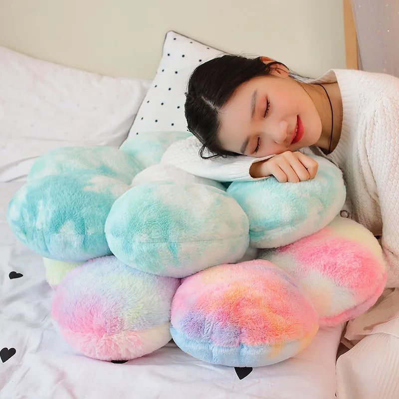 A close-up of a person resting their head on a fluffy pink and yellow sunflower plush flower cushion in a white bed.