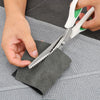 A hand is using professional pinking shears with an ergonomic grip to cut fabric on a gray cloth.