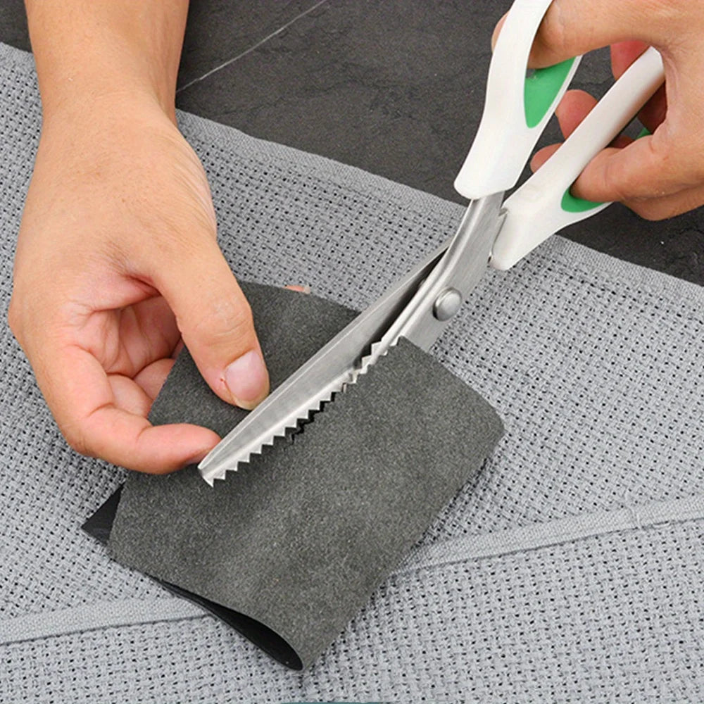 A hand is using professional pinking shears with an ergonomic grip to cut fabric on a gray cloth.
