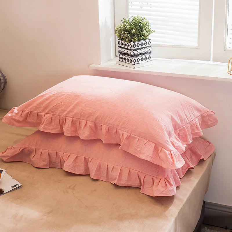 A set of two soft pink plaid pillowcases with ruffled edges displayed on a light-colored surface.