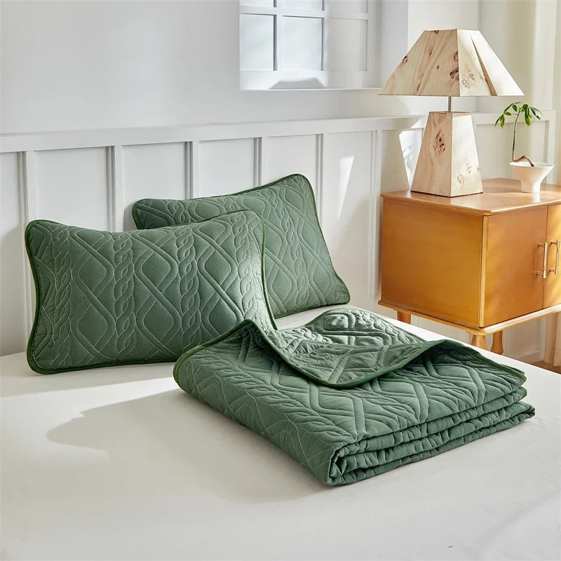 A set of olive green quilted bedding, including pillows and a folded blanket, displayed on a white bed.