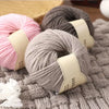 A stack of pink and gray wool yarn skeins resting on a knitted gray fabric.