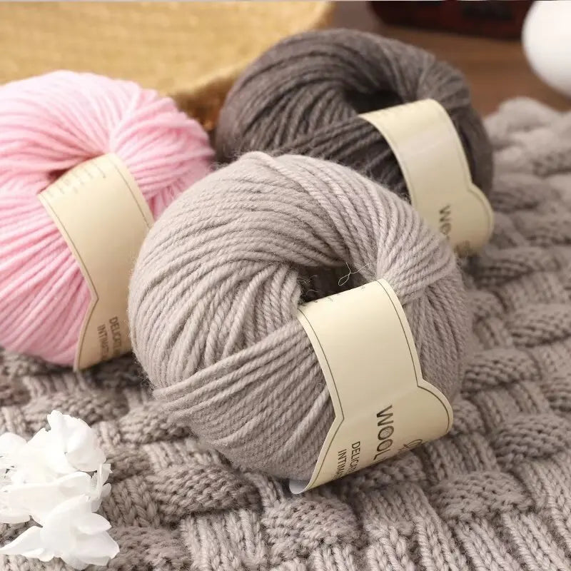 A stack of pink and gray wool yarn skeins resting on a knitted gray fabric.