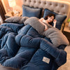 A woman is relaxing under a large, plush double-sided fleece blanket in deep blue velvet and gray textures.