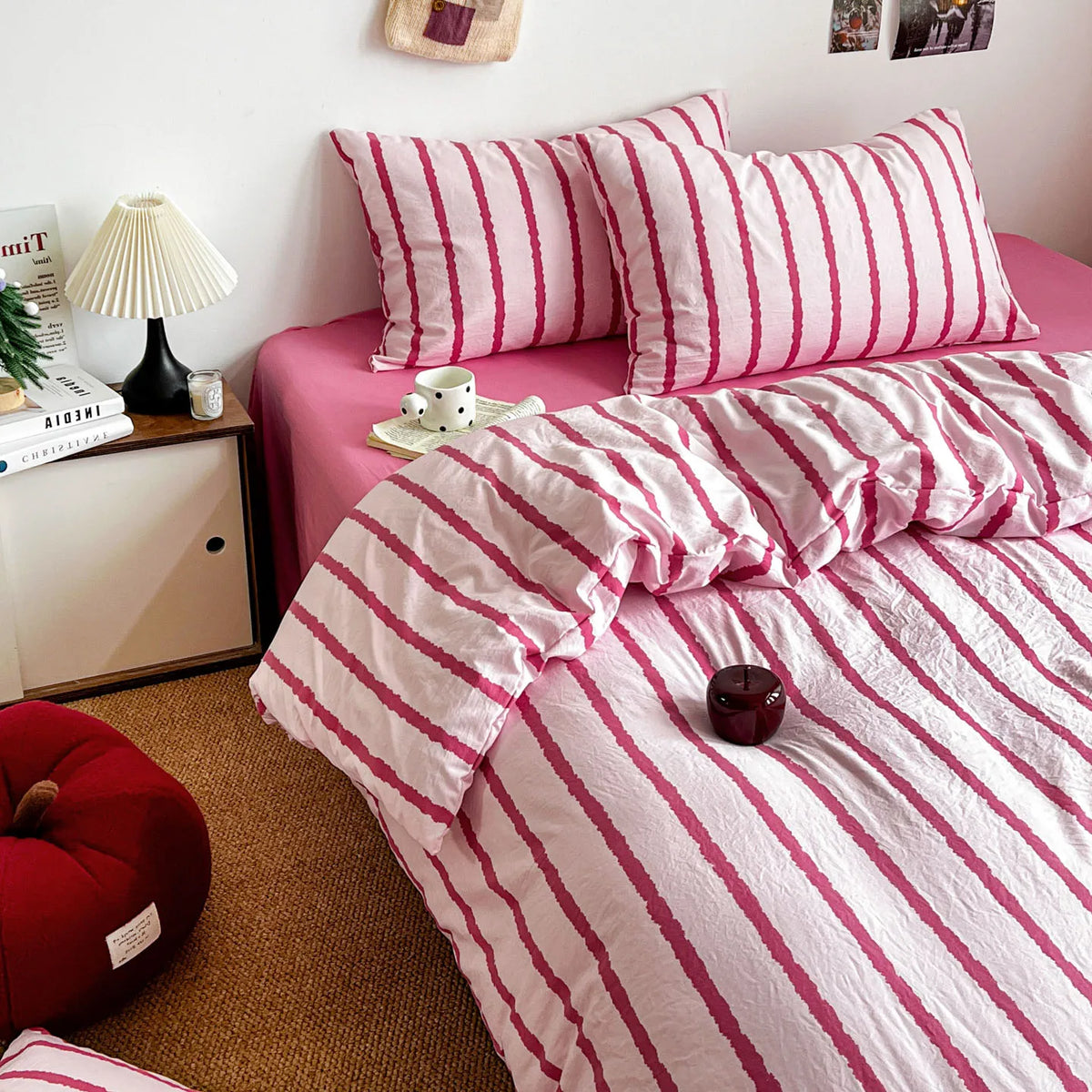 A pink striped duvet cover set with matching pillowcases is displayed on a bed, surrounded by pillows and a bedside lamp.