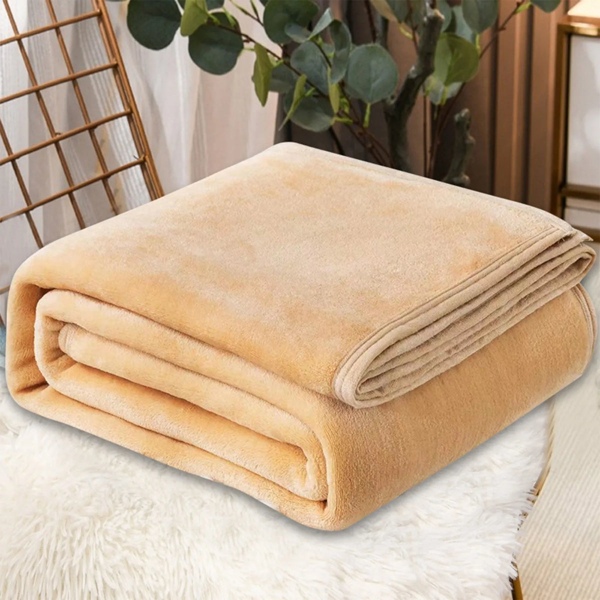 A folded tan coral fleece throw blanket resting on a white fluffy surface.