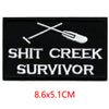 Black embroidered patch featuring a crossed fork and knife design above the text SHIT CREEK SURVIVOR