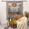 A bohemian geometric throw blanket hangs on a wall, displayed next to a woven chair and dried grasses.