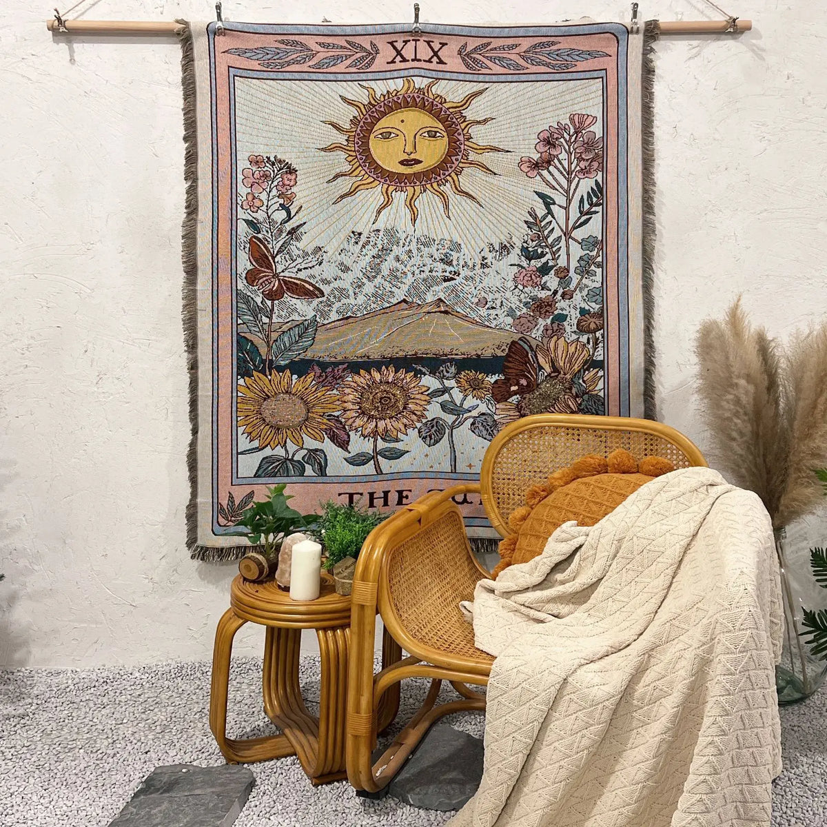 A bohemian geometric throw blanket hangs on a wall, displayed next to a woven chair and dried grasses.