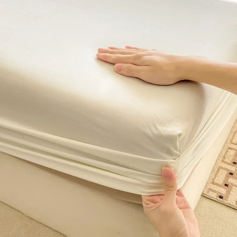 A hand is adjusting a white fitted bed sheet on a mattress.