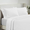 White luxury bedding set featuring striped pillows and a fitted sheet on a light upholstered bed.