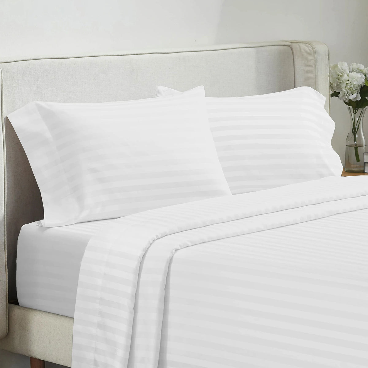 White luxury bedding set featuring striped pillows and a fitted sheet on a light upholstered bed.