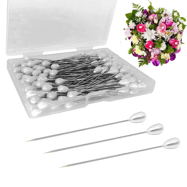 A clear plastic box containing silver pearl teardrop corsage boutonniere pins and several individual pins.