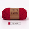 A skein of red yarn labeled Sweet Candy Yarns, shown flat on a white surface.
