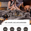A woman relaxing on a gray ice silk blanket set with pillows and a decorative pouch.