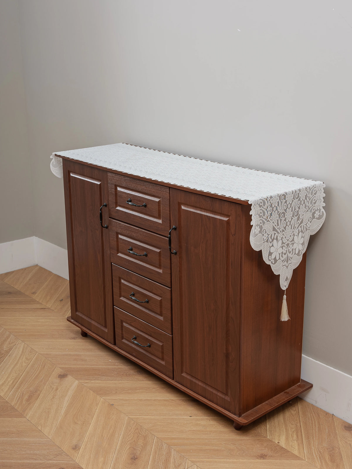 A dark wood cabinet with a white embroidered lace table runner on top, used for dining or furniture accents.