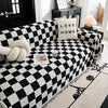 A black and white checkerboard sofa slipcover with a cream pillow and a white knitted accent.