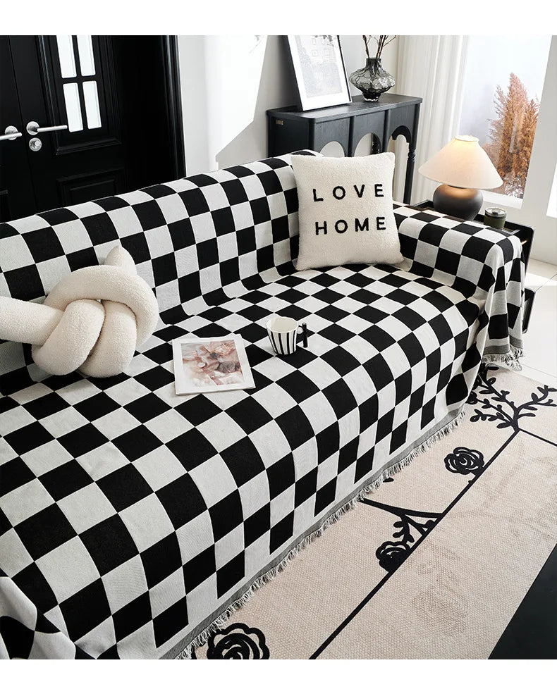 A black and white checkerboard sofa slipcover with a cream pillow and a white knitted accent.
