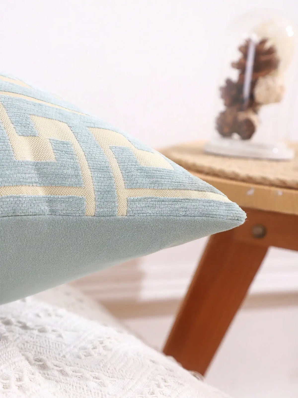 A close-up of a light blue throw pillow cover with beige geometric embroidery resting on a wooden surface.