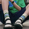 A close-up of a person's legs and feet wearing white and green striped crew socks and black sandals.