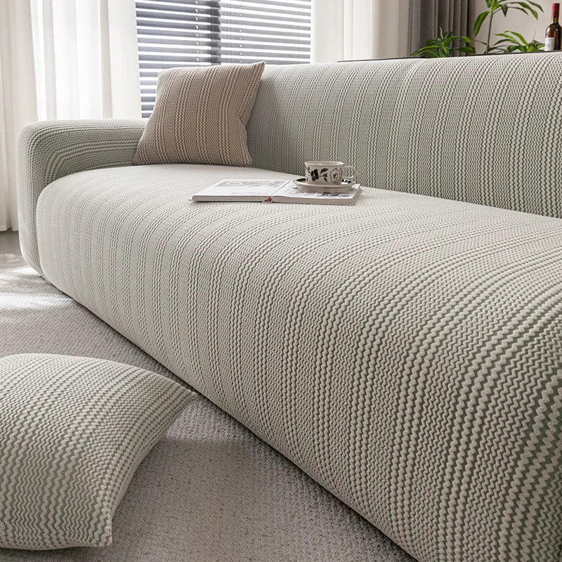 A light beige protective anti-scratch sofa slipcover with textured fabric and throw pillows on a modern sofa.