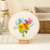 A circular embroidery hoop displays a colorful floral design featuring yellow and purple flowers and blue accents.