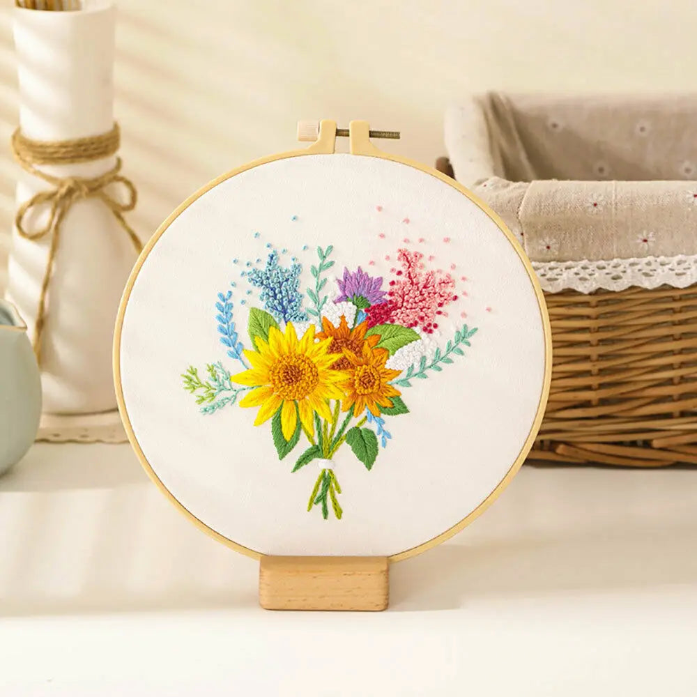 A circular embroidery hoop displays a colorful floral design featuring yellow and purple flowers and blue accents.