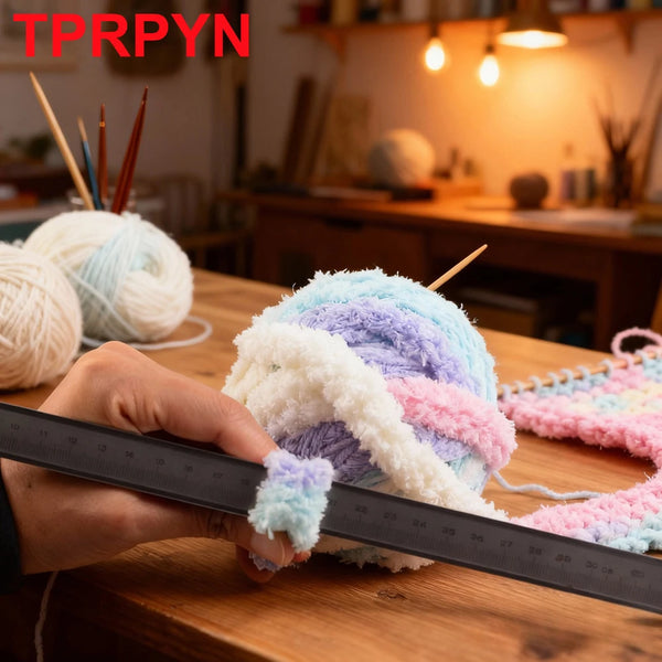 A hand measures a ball of multicolored chunky chenille yarn on a wooden table.