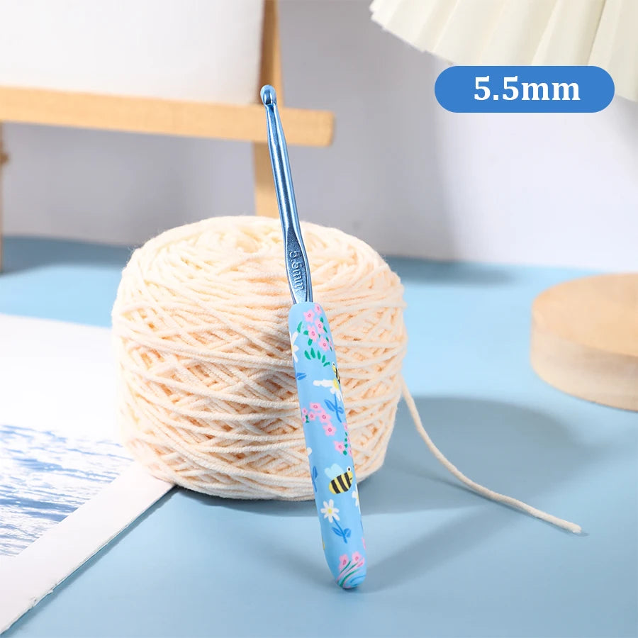 A blue ergonomic crochet hook with a 5.5mm tip is shown next to a ball of cream-colored yarn on a light blue surface.