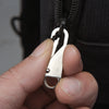 A hand holds a silver zipper slider puller repair kit component against a black fabric background.
