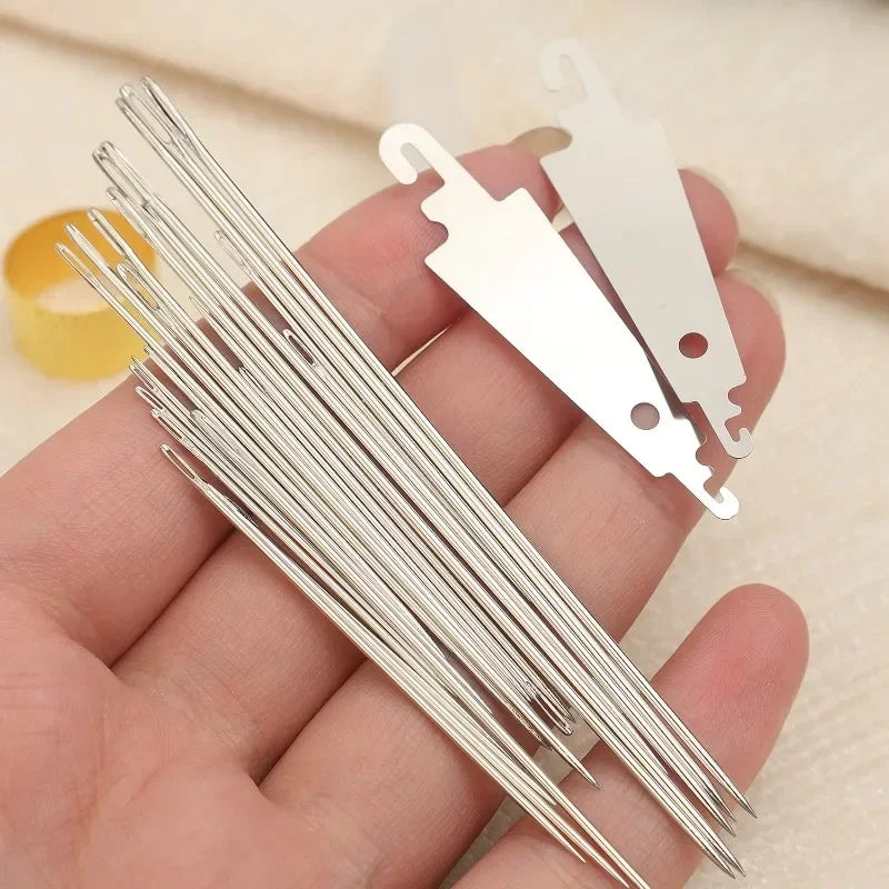 A hand holds a set of stainless steel big-eye sewing needles and a pair of needle holders.