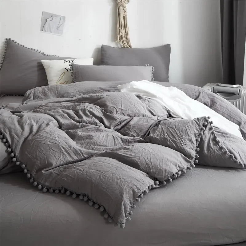 A gray duvet cover set with pom-pom decoration on a bed.