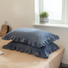 A set of two soft blue washed cotton pillowcases with ruffled edges resting on a light brown surface.