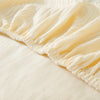 A close-up of a cream-colored stretchable sofa cover with a ribbed line pattern, showing the gathered hemline.