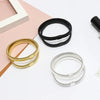 Three adjustable metal sleeve garters for men in gold, black, and silver lying on a pink surface.