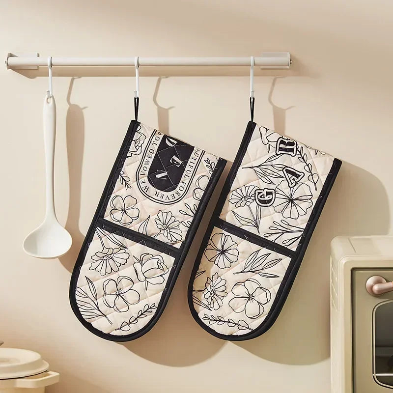 Two floral heat-resistant oven mitts are hanging on a rack against a beige wall.