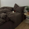 A dark brown duvet cover set with matching pillows and a folded blanket on a bed.