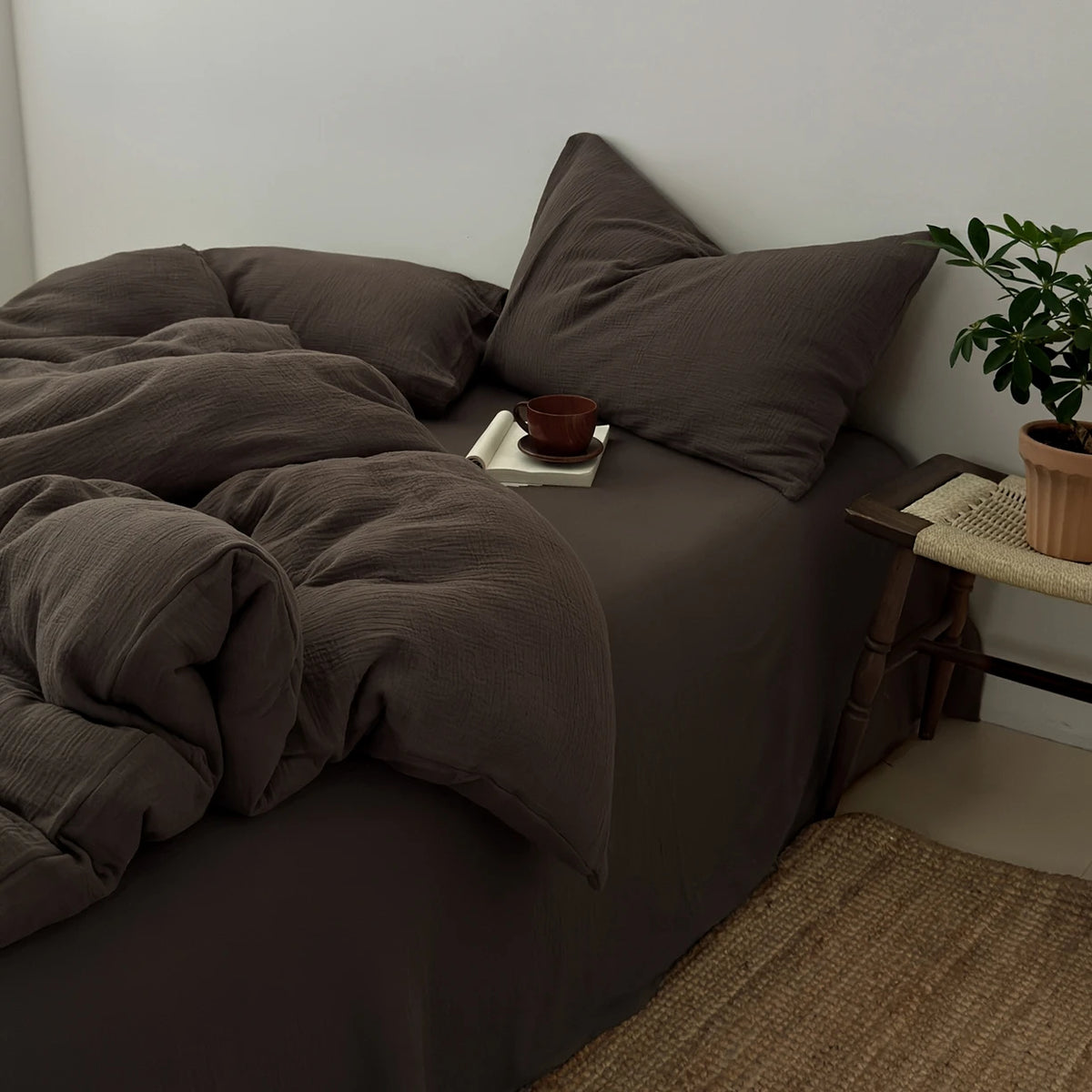 A dark brown duvet cover set with matching pillows and a folded blanket on a bed.