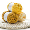 A stack of thick, golden yellow velvet yarn balls wrapped in white labels resting on a woven mat.