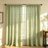 A pair of light green floral print curtains hanging in a window, filtering soft sunlight onto a wooden floor.