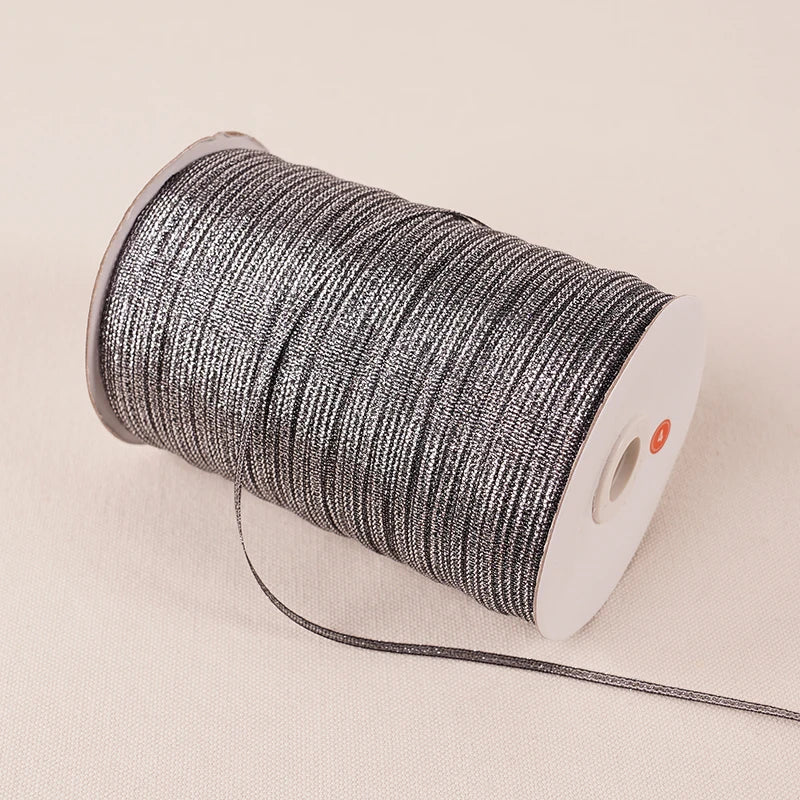 A roll of 10-meter gold and silver glitter satin ribbon with a white core and black thread.