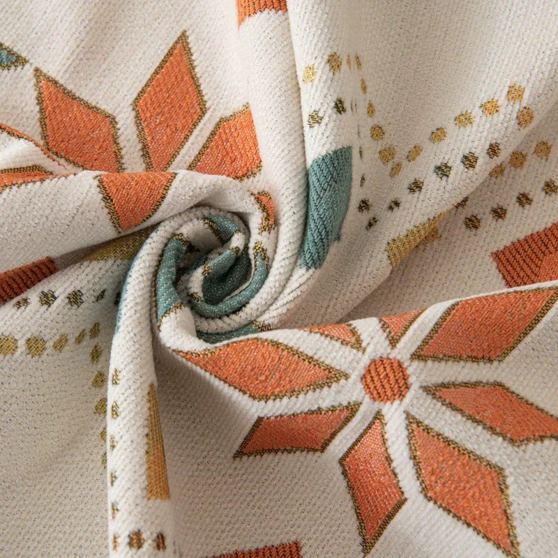 A close-up of a beige fabric with an orange floral pattern and gold accents, rolled into a swirl.