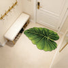 A green leaf-shaped quick-dry bathroom mat with a rubber backing placed on a tiled floor.