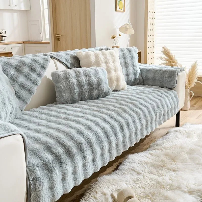 A light gray plush rabbit sofa cushion draped over a sofa, next to a white faux fur rug.