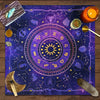 A dark blue tarot card tablecloth featuring a zodiac wheel and celestial symbols with tarot cards and a candle.