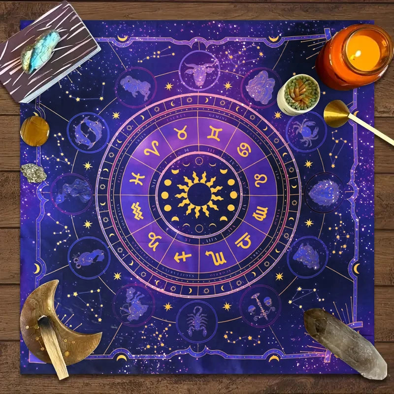 A dark blue tarot card tablecloth featuring a zodiac wheel and celestial symbols with tarot cards and a candle.