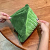 A hand holds a green leaf-shaped absorbent microfiber towel on a wooden surface.