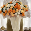 A hand knitted floral rose bouquet is held by a person, featuring orange and white flowers, with a cream colored throw blanke