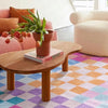 A wooden coffee table sits on a colorful geometric rug in a bright living room setting.