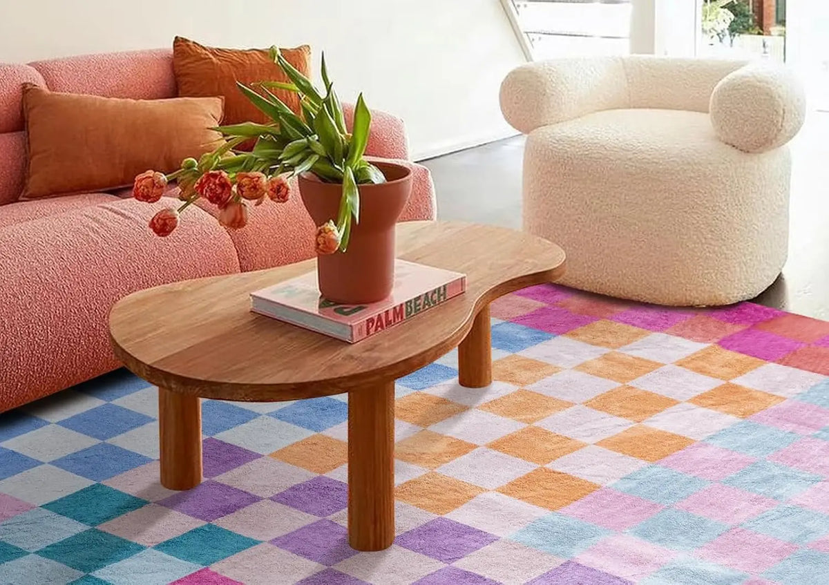 A wooden coffee table sits on a colorful geometric rug in a bright living room setting.